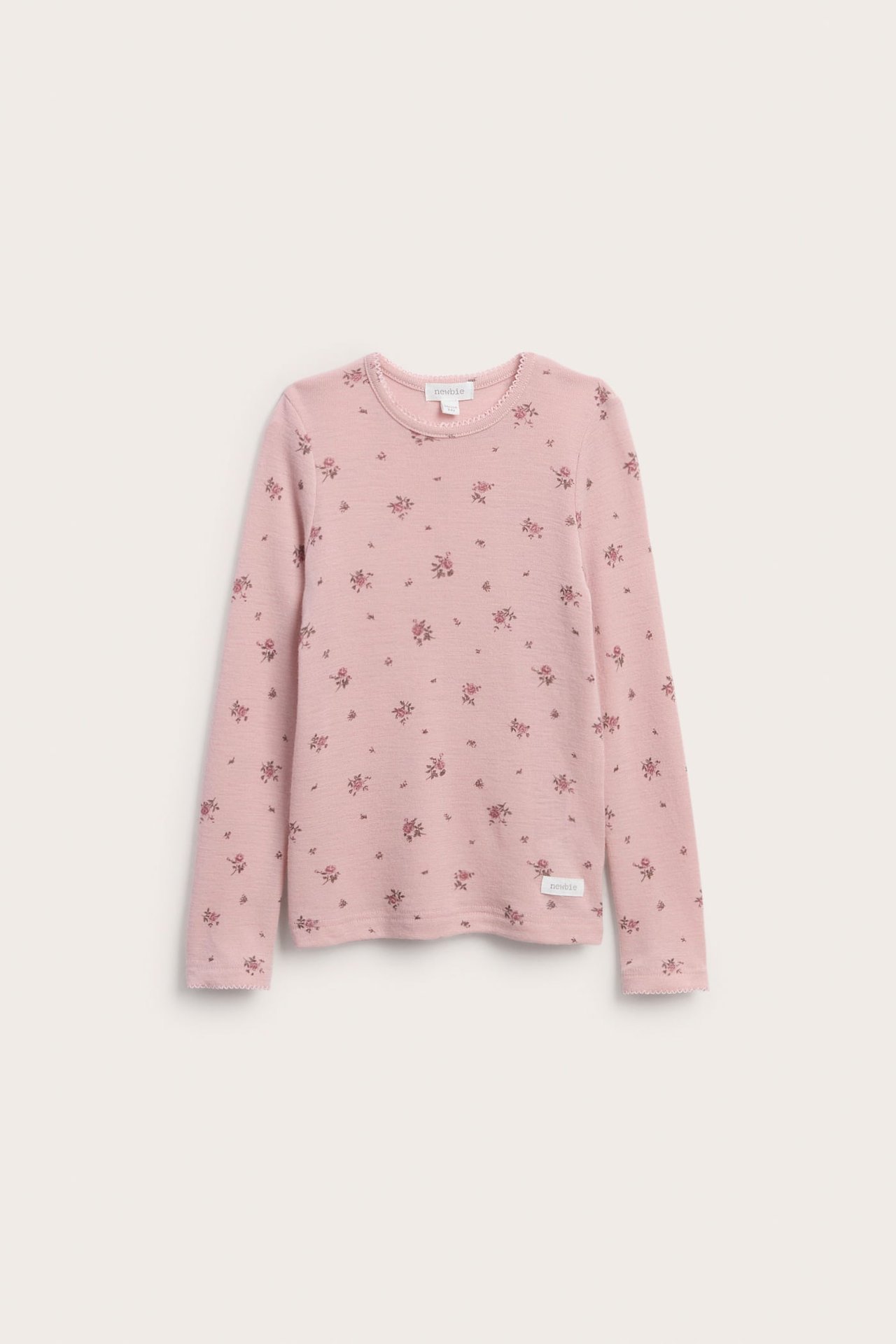 Front view of a kid's pink long-sleeved top with a small floral print and scalloped trim.