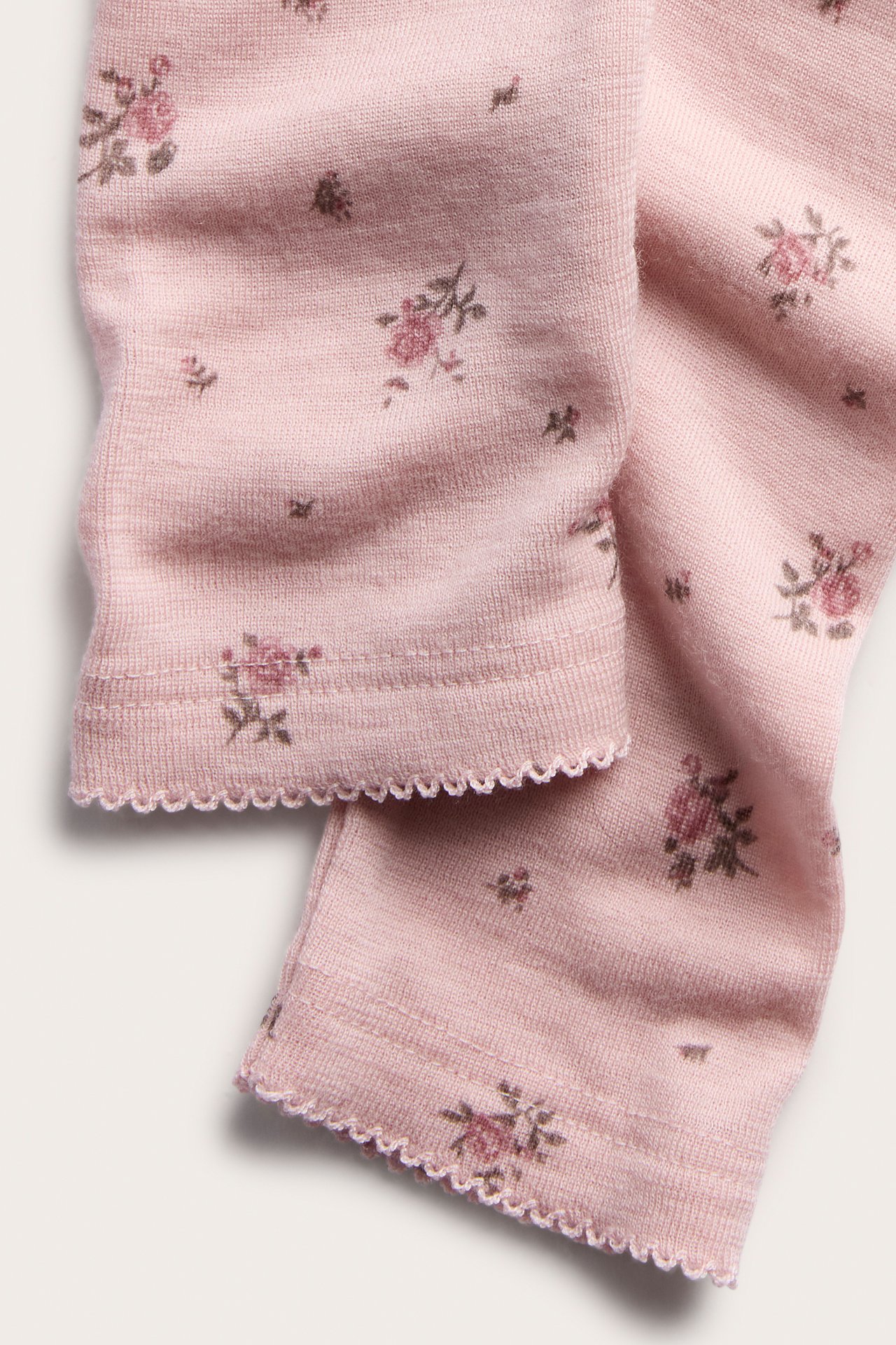 Close-up of pink baby leggings with a small floral print and scalloped cuffs.