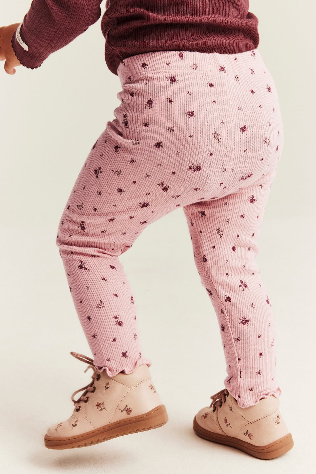 Side view of kid wearing pink floral ribbed leggings, maroon ribbed top, and light pink floral shoes.