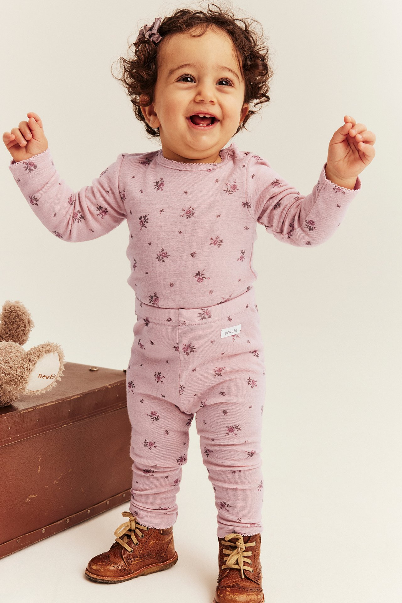 Front view of baby wearing a pink floral long-sleeved top and matching leggings set with brown lace-up boots.