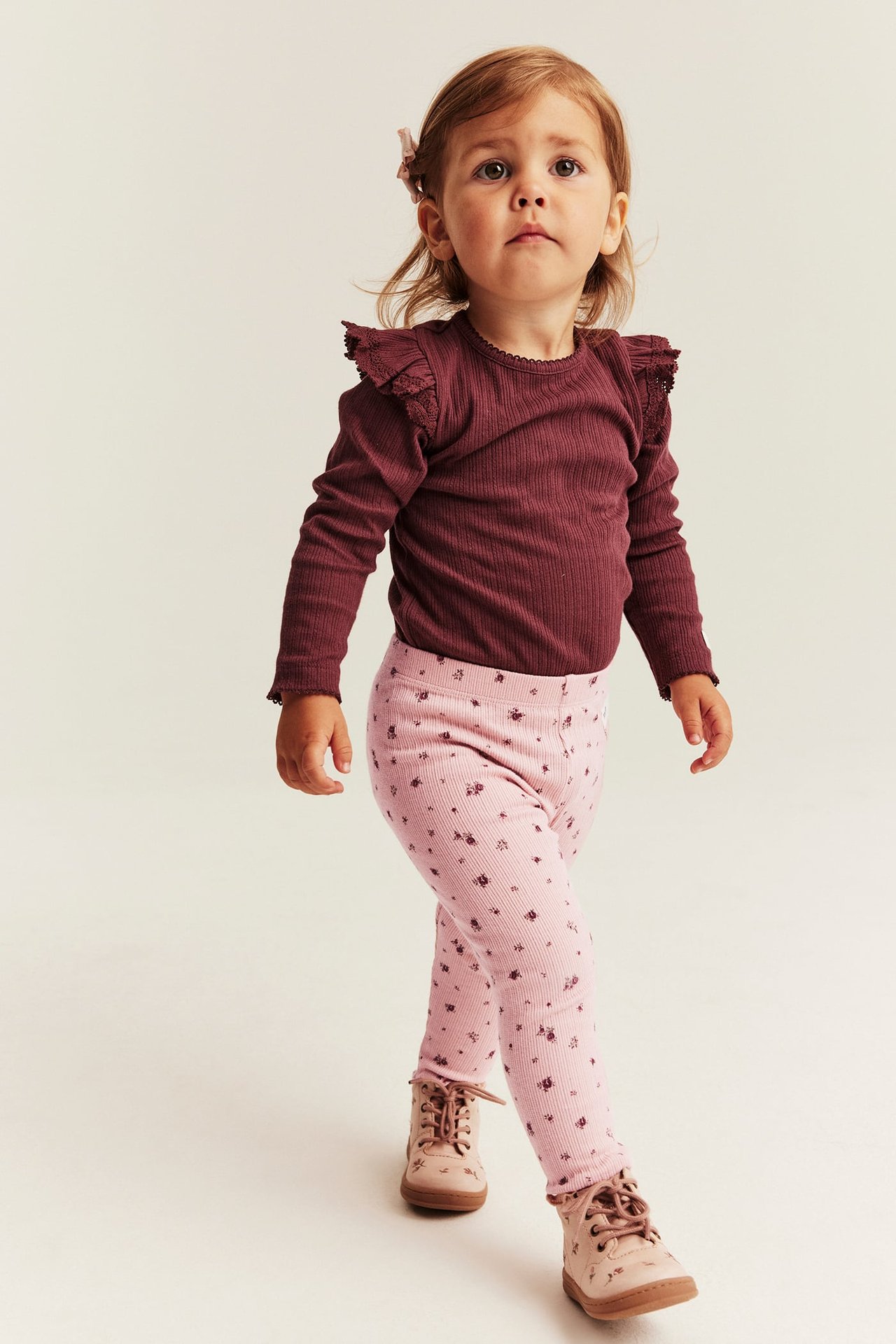 Front view: Baby girl in pink floral ribbed leggings, burgundy top, and light brown boots.