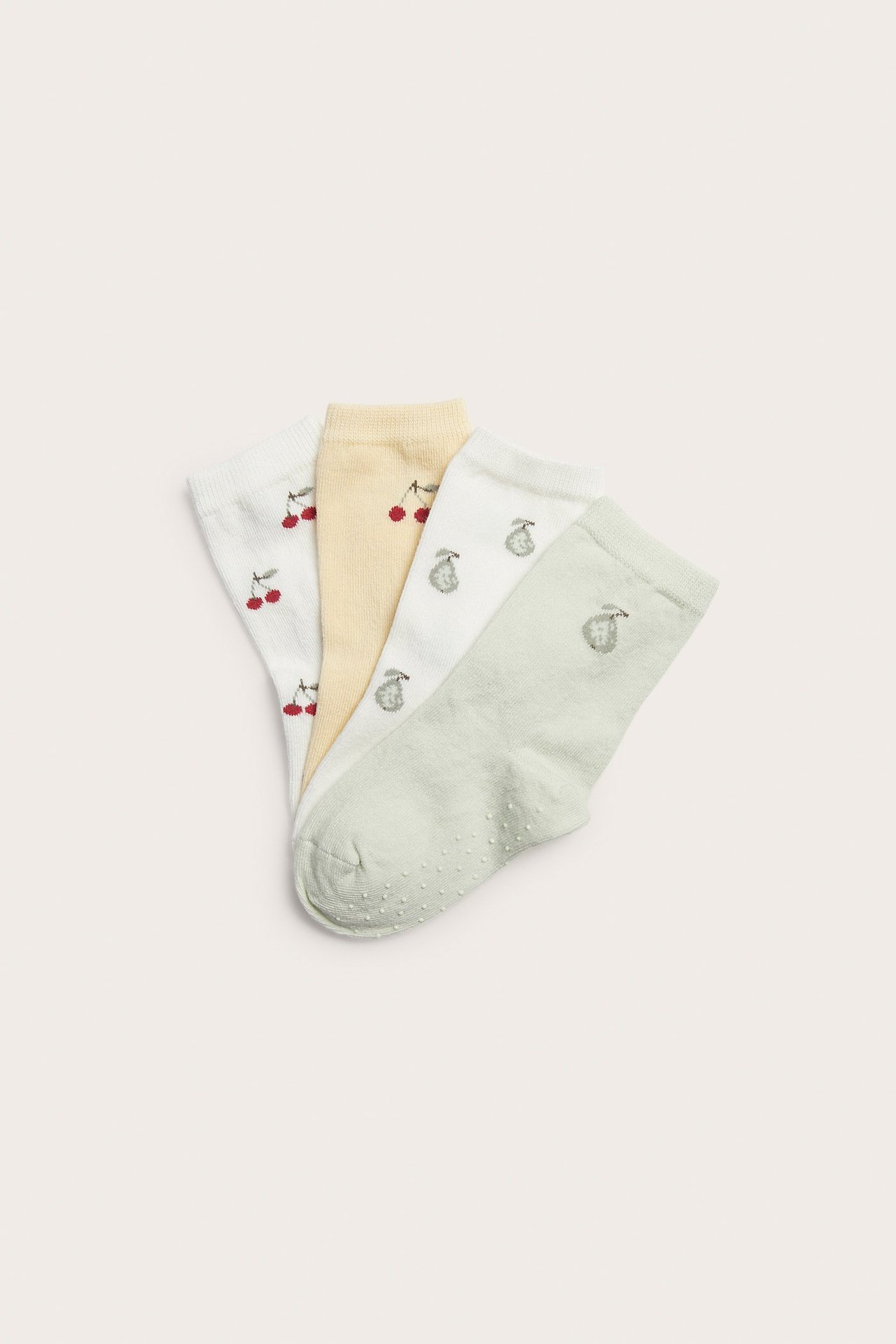 Nahaufnahme von vier gemusterten Baumwoll-Babysocken in Off-White, Gelb und Grün, mit Antirutschsohle.
