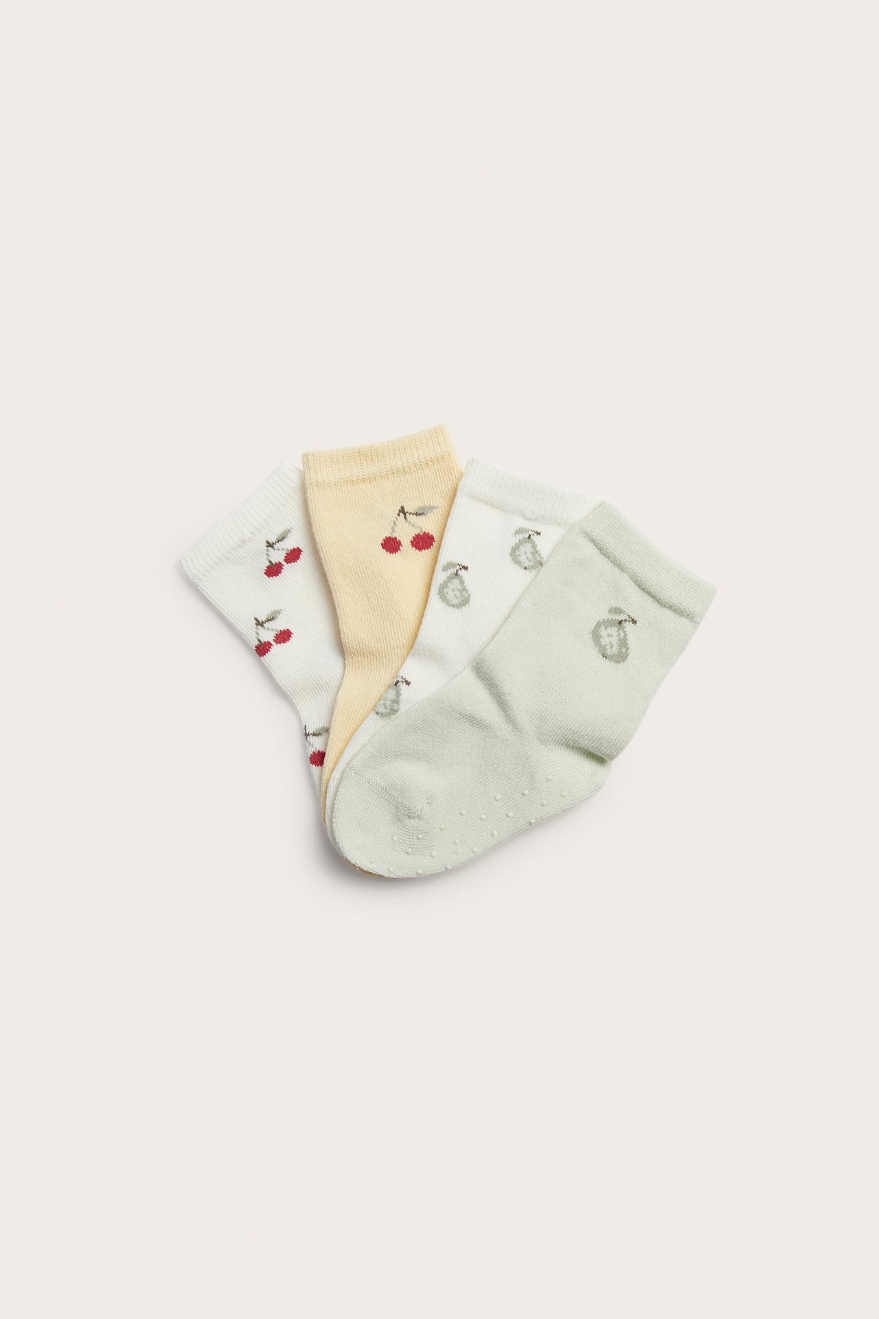 Draufsicht auf vier gemusterte Kindersocken: cremefarben Kirsche, hellgelb Kirsche, cremefarben Birne, hellgrün Antirutsch.