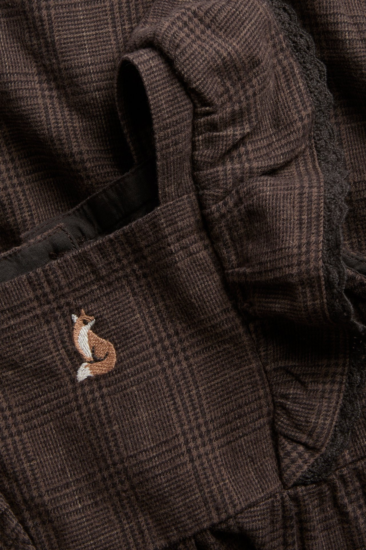 Close-up of a brown plaid garment with an embroidered fox and dark lace trim.