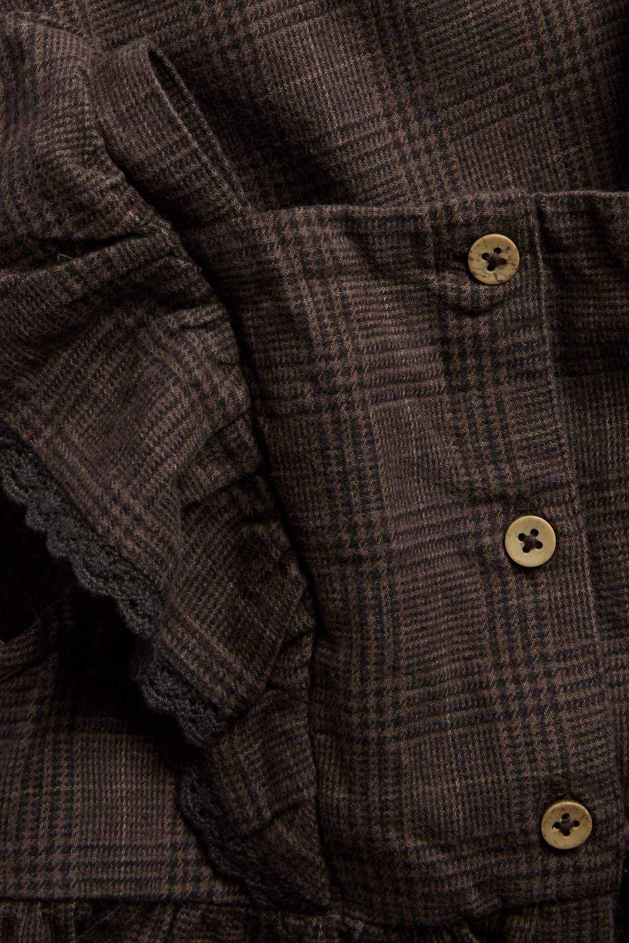 Close-up of a brown plaid garment with ruffles and round wooden buttons.