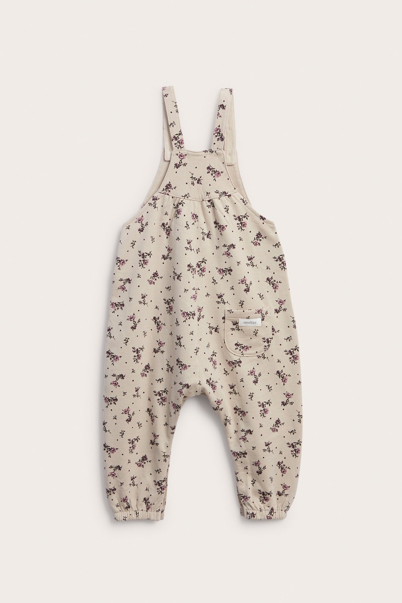 Front view of baby beige floral print overalls with adjustable straps and a front pocket.