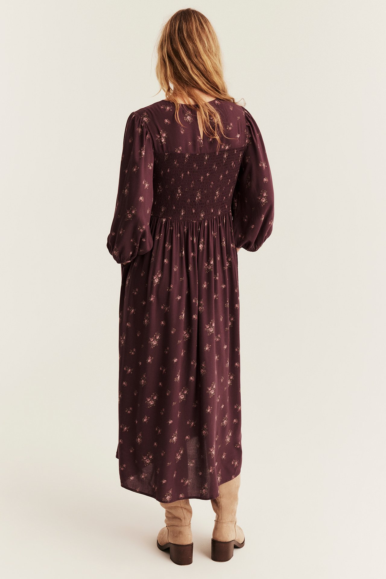 Back view of a woman in a plum floral smocked midi dress and light brown boots.
