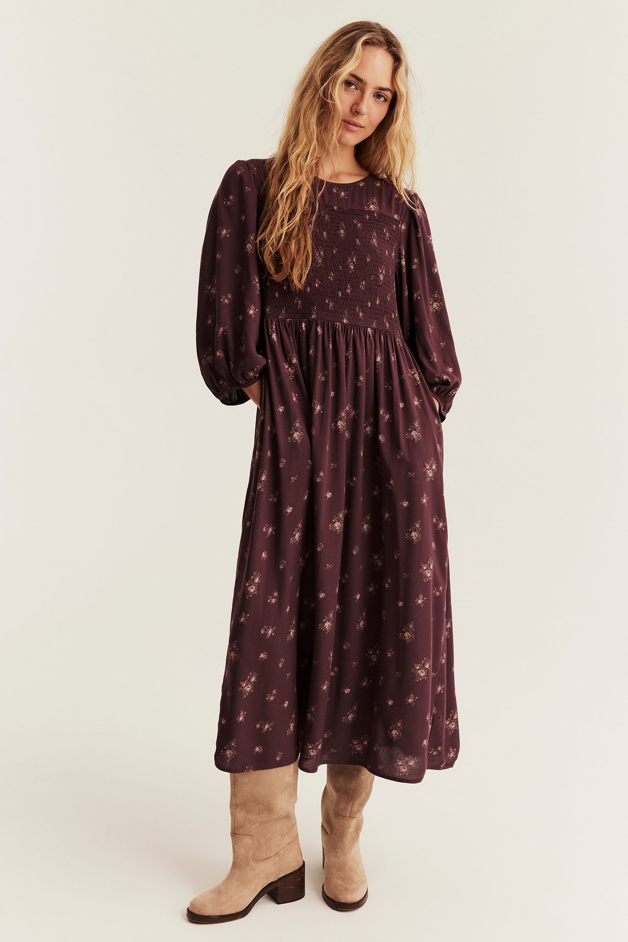 Front view of a woman wearing a dark purple floral midi dress with a smocked bodice and beige suede boots.