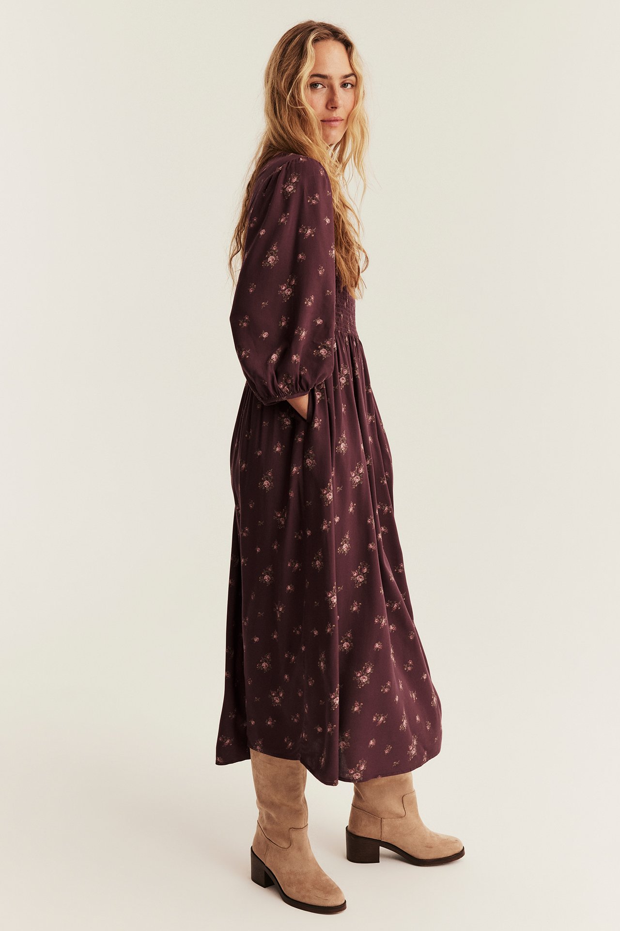 Side view of a woman wearing a dark purple floral print midi dress with puff sleeves and beige boots.