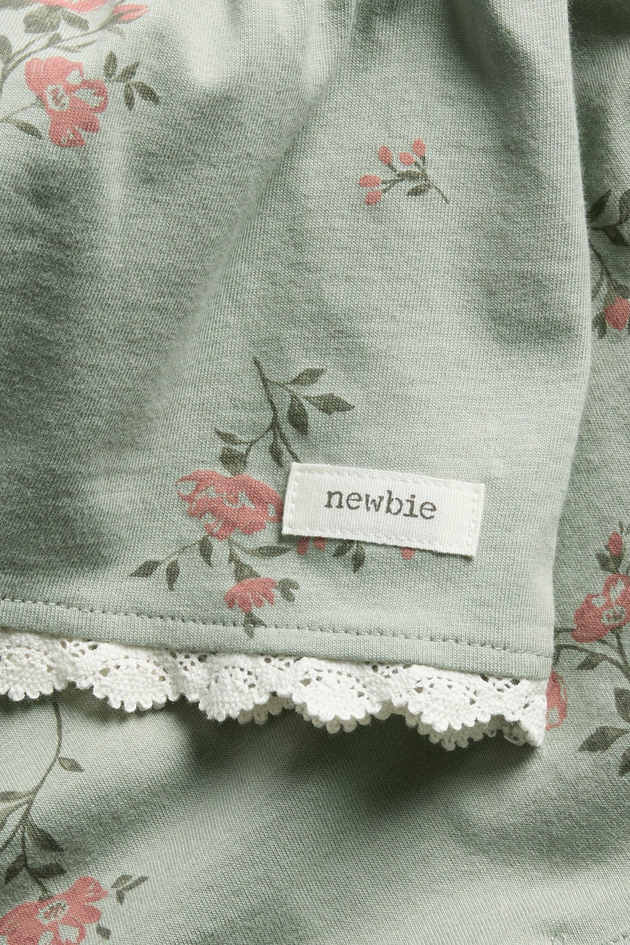 Close-up of a green cotton top with pink floral pattern and white lace trim.