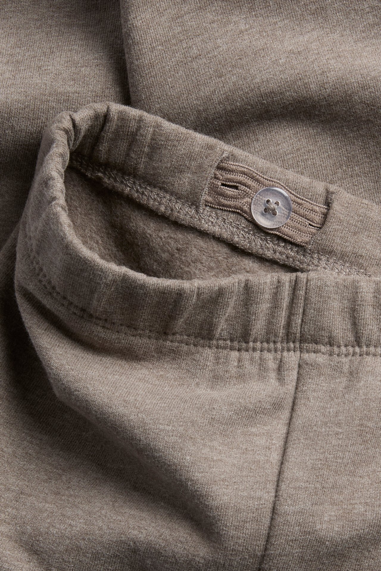 Close-up of light brown kids' pants with an adjustable elastic waistband and a button.
