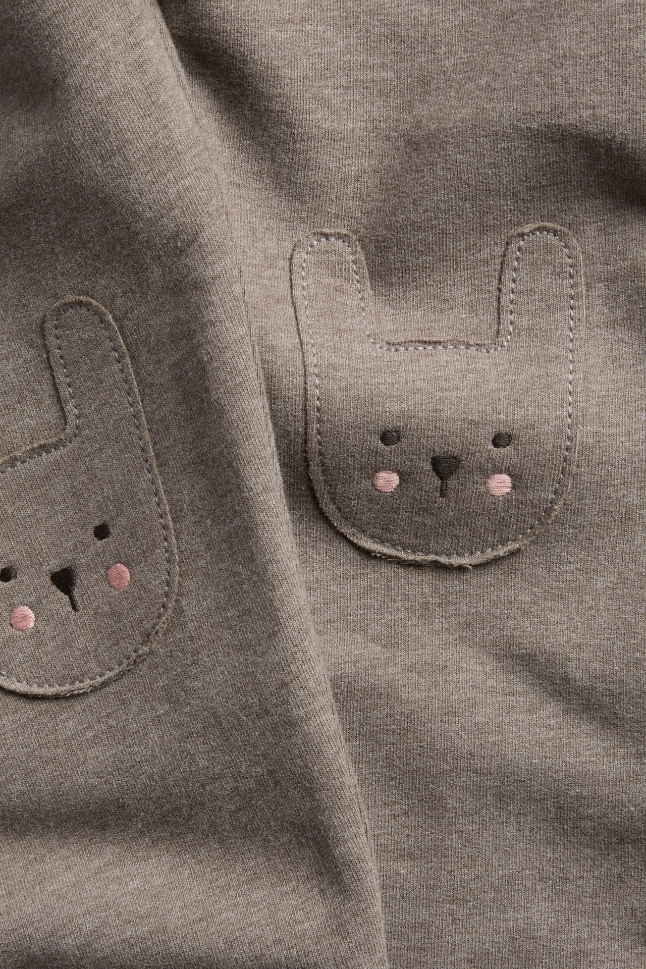 Close-up of a brown jersey fabric with two bunny face pockets, featuring black eyes and pink cheeks.