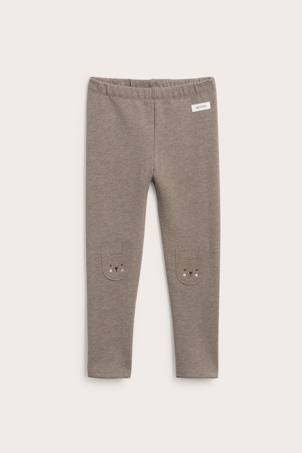 Front view of taupe baby leggings with bunny ear patches on knees and a 'newbie' label.