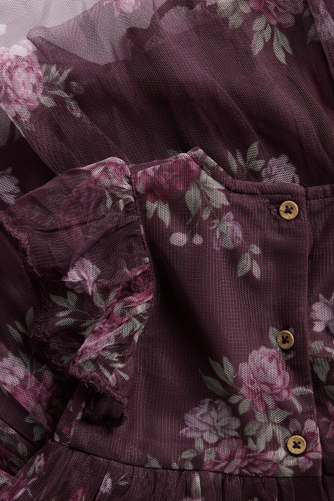 Nahaufnahme eines dunkelvioletten Mesh-Kleides mit Blumenmuster, Rüschen und Holzknöpfen.