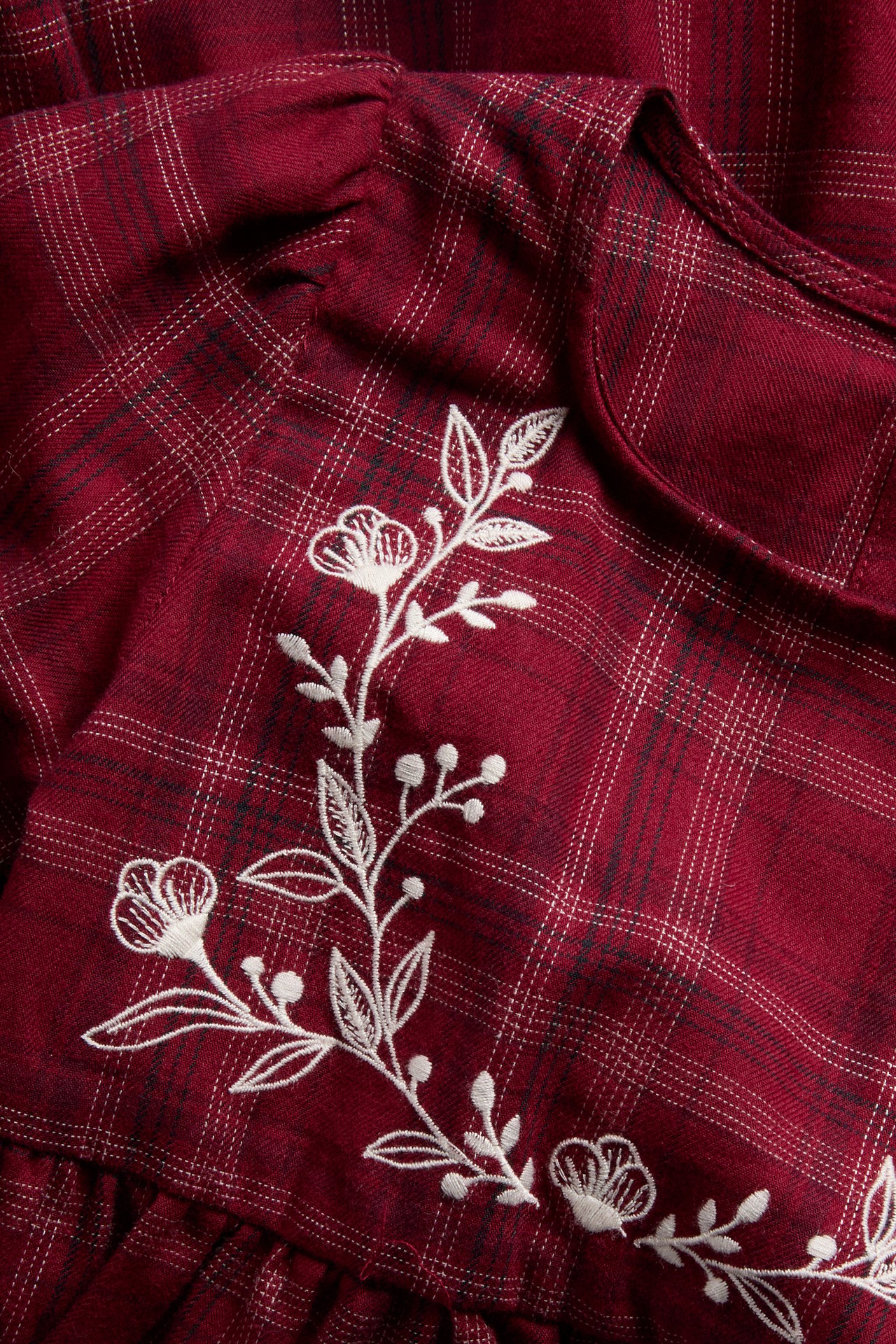Close-up of a dark red flannel plaid top with white floral embroidery.