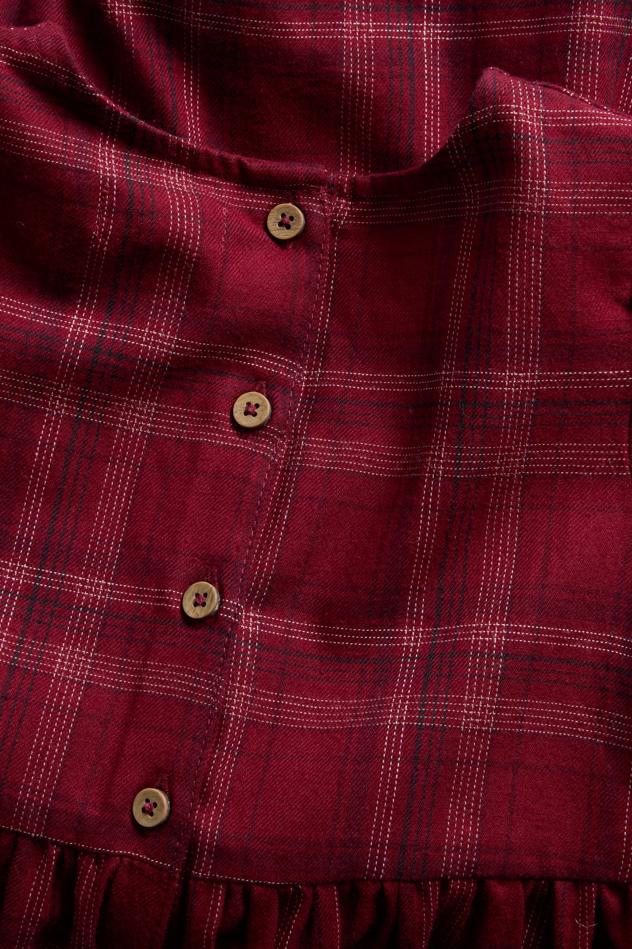 Close-up front view of a dark red plaid garment with white lines and wooden buttons.