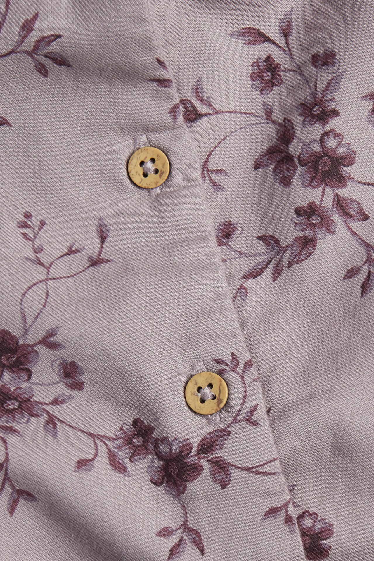 Close-up of a light purple woven fabric with dark floral print and two beige buttons.