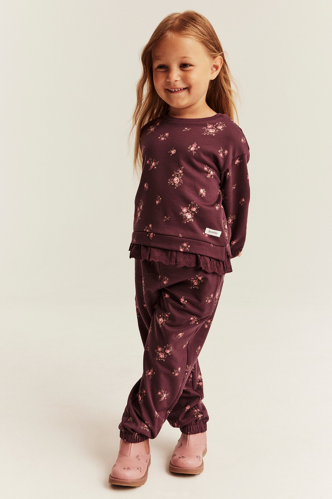Front view of a kid in a burgundy floral long-sleeve sweatshirt and matching joggers, with pink floral boots.
