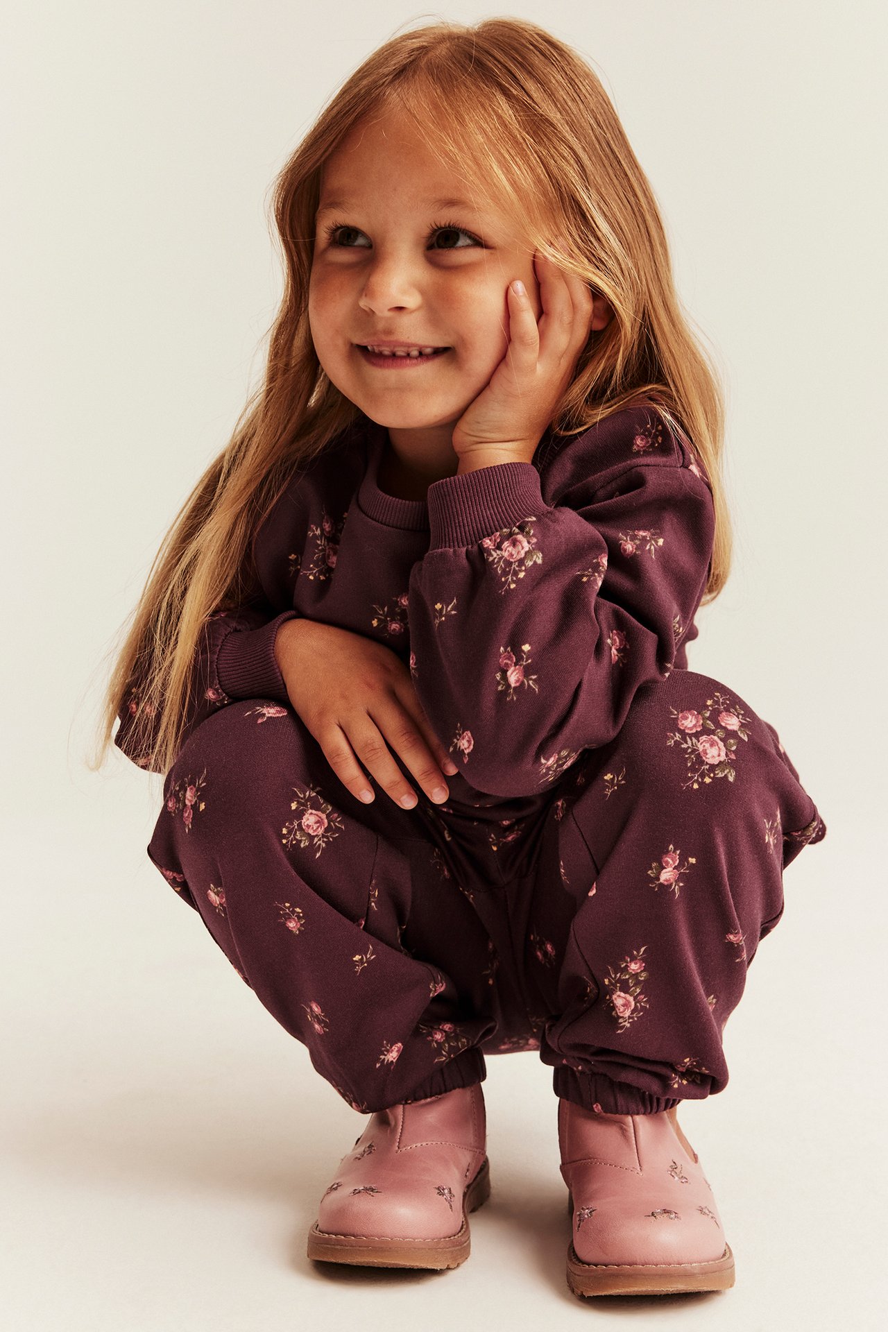 Front-angled view of a kid in a dark purple floral top and matching pants set with pink boots.