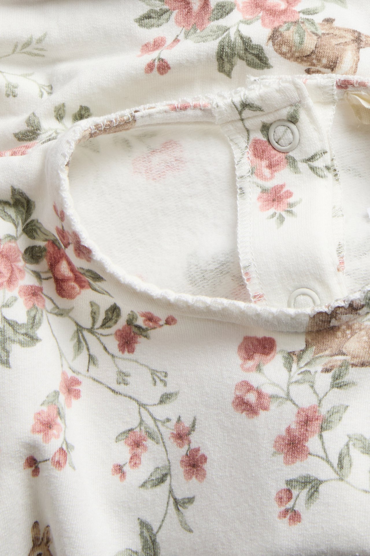 Close-up of an off-white, thicker jersey dress with pink floral and deer pattern and snap buttons.