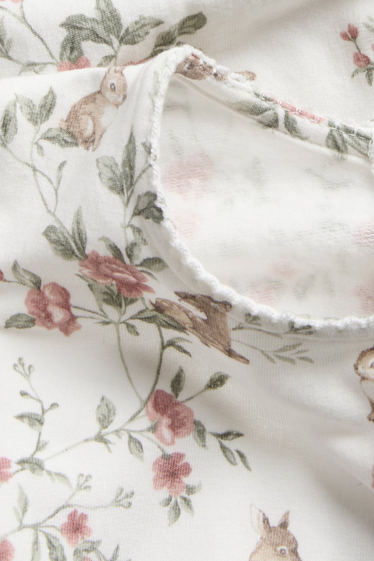 Close-up of an off-white jersey dress with a pattern of light pink flowers and brown rabbits.