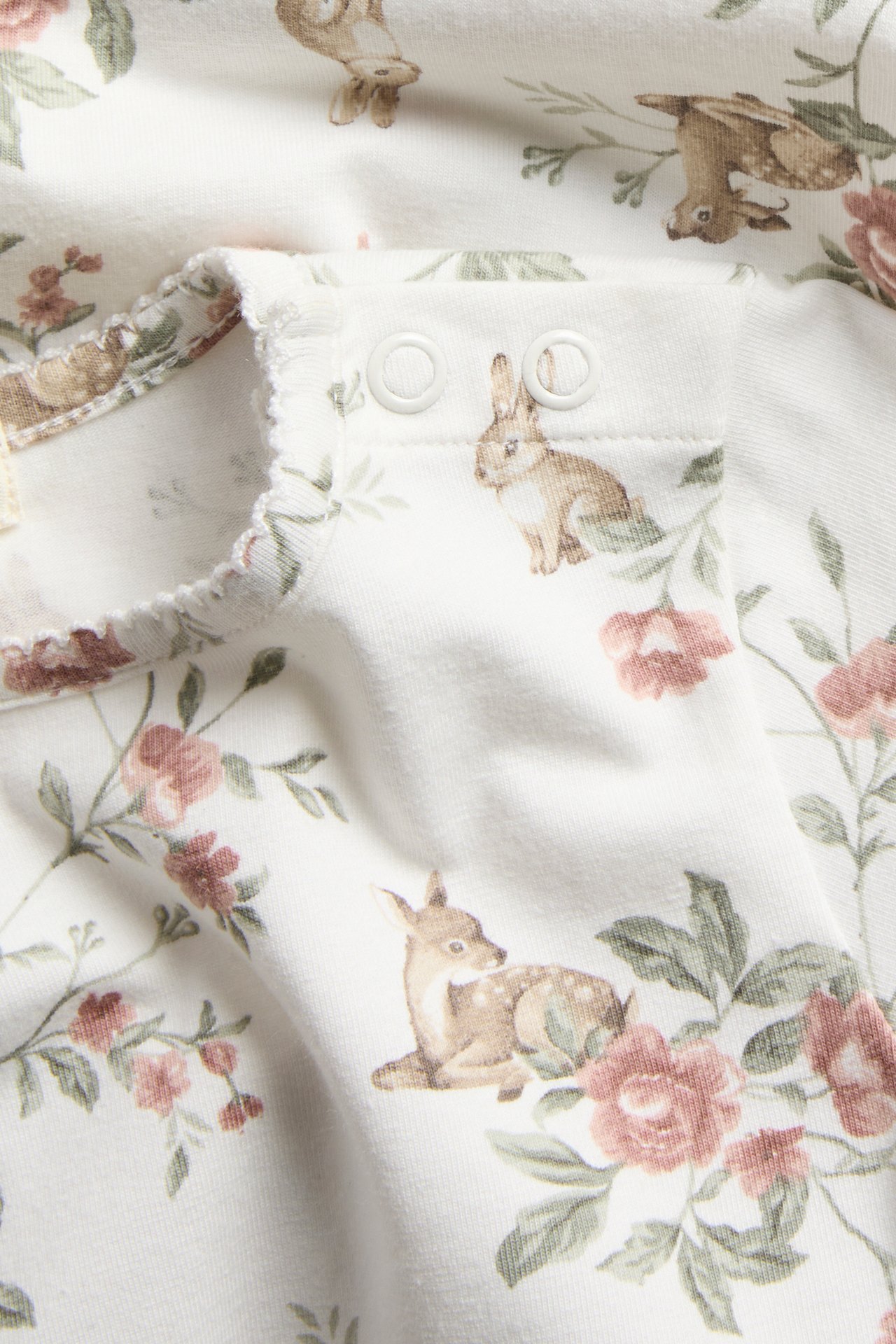 Close-up of an off-white baby long-sleeved body with deer and floral print, picot trim, snap buttons.