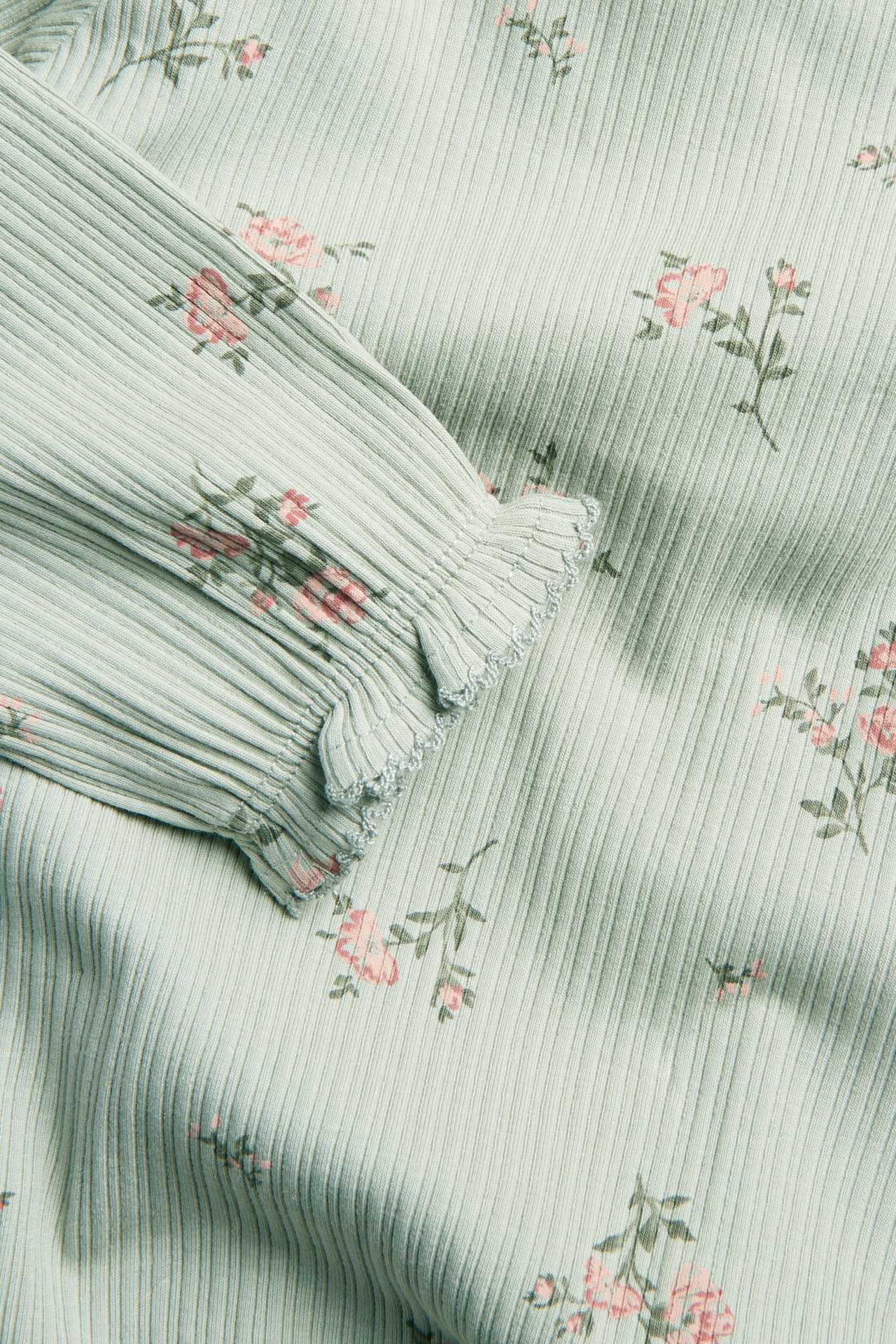 Close-up of a baby's ribbed light green floral body with a ruffled picot cuff.