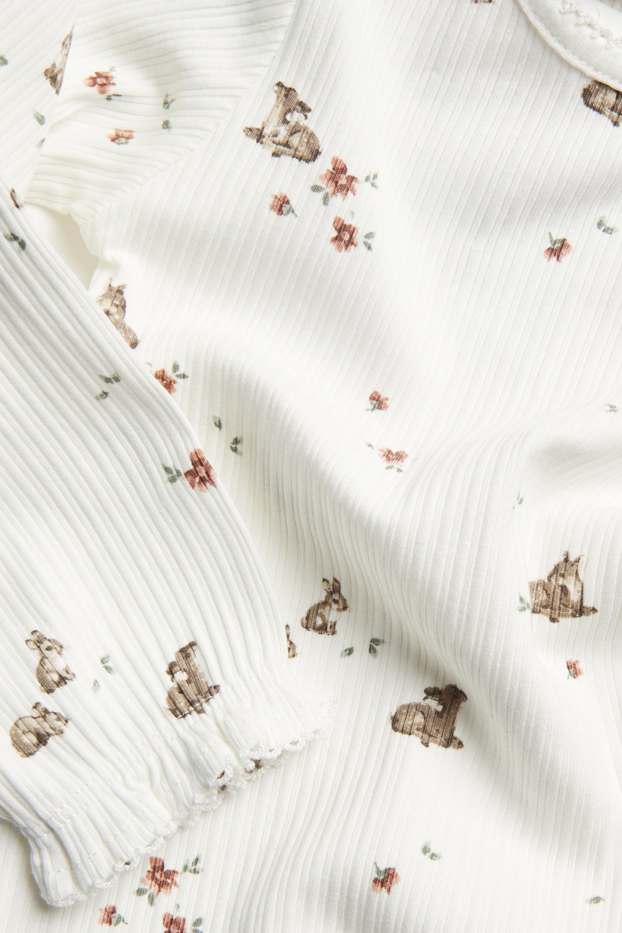 Close-up of an offwhite ribbed baby long-sleeved bodysuit with deer and floral print, plus ruffles.