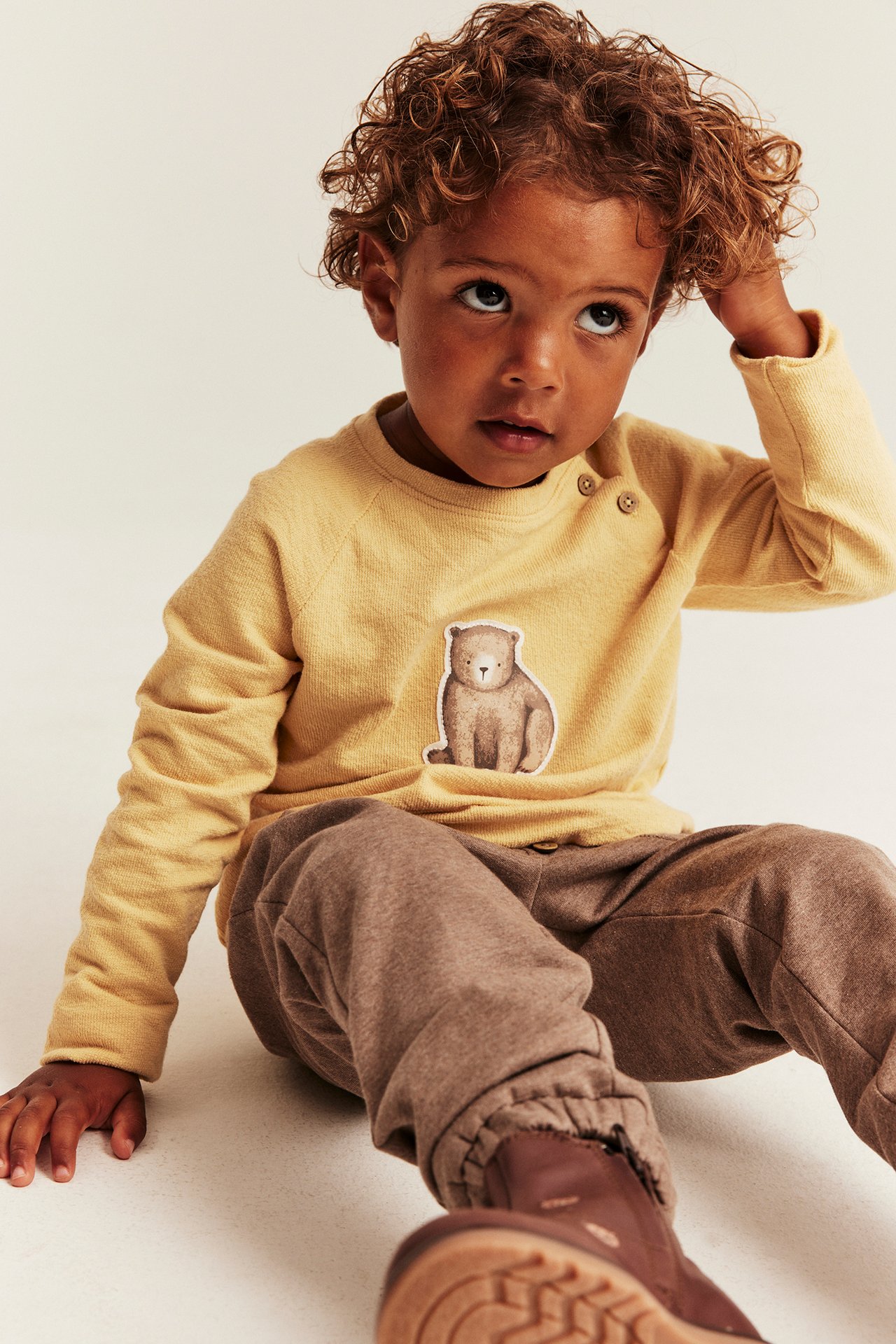 Front view of a kid wearing a yellow long-sleeve top with a bear print and brown sweatpants.