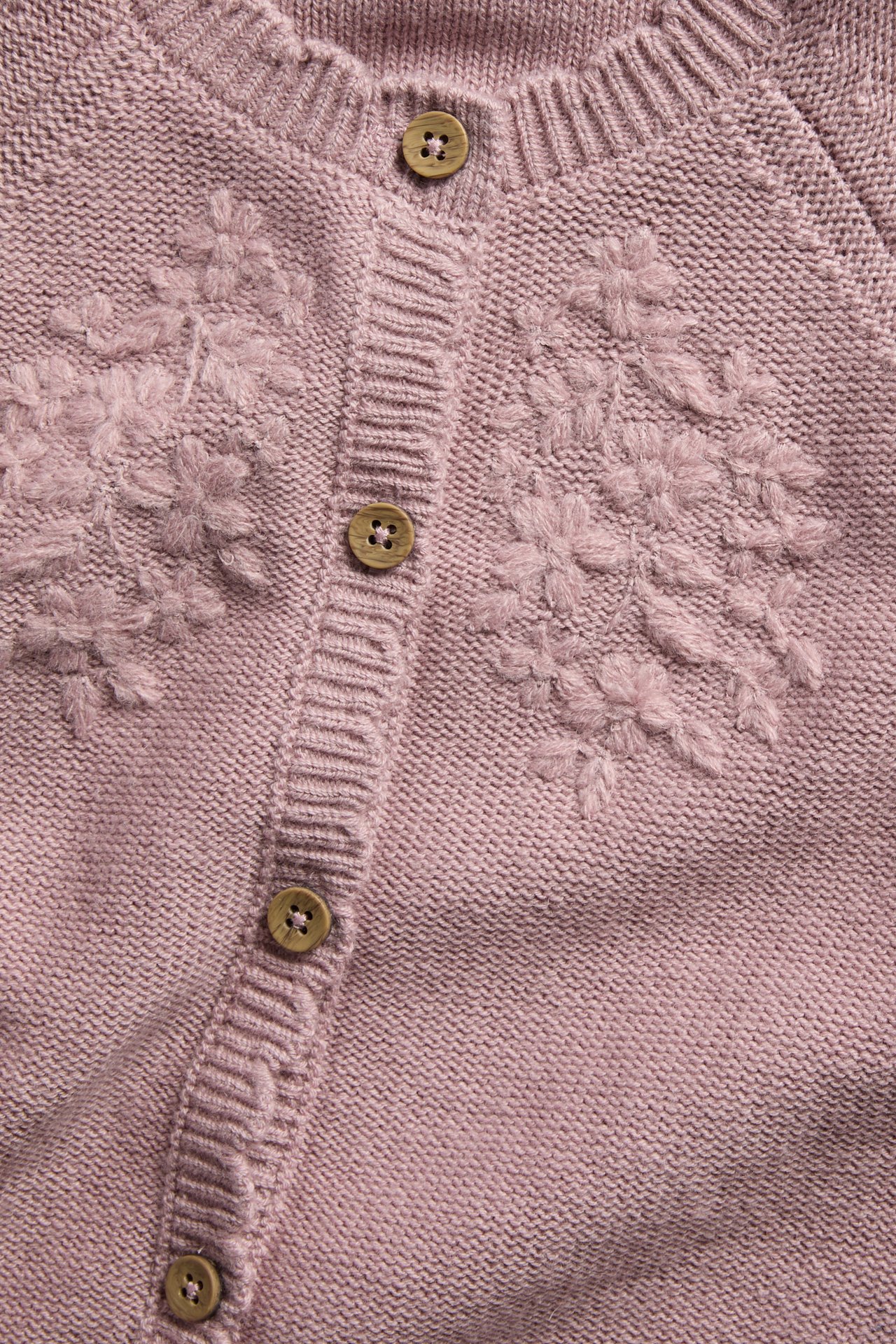 Nahaufnahme einer altrosafarbenen Strickjacke mit Blumenstickerei und Holzknöpfen.