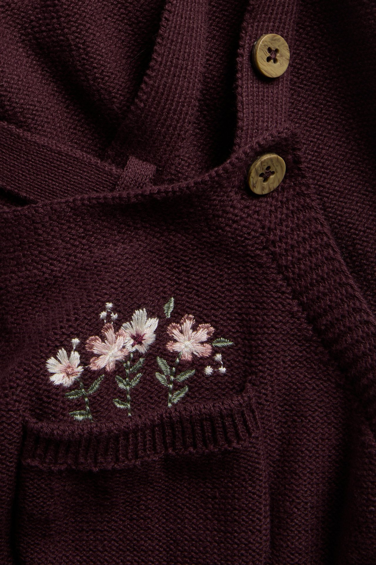 Close-up of a burgundy knit garment with floral embroidery and two wooden buttons.