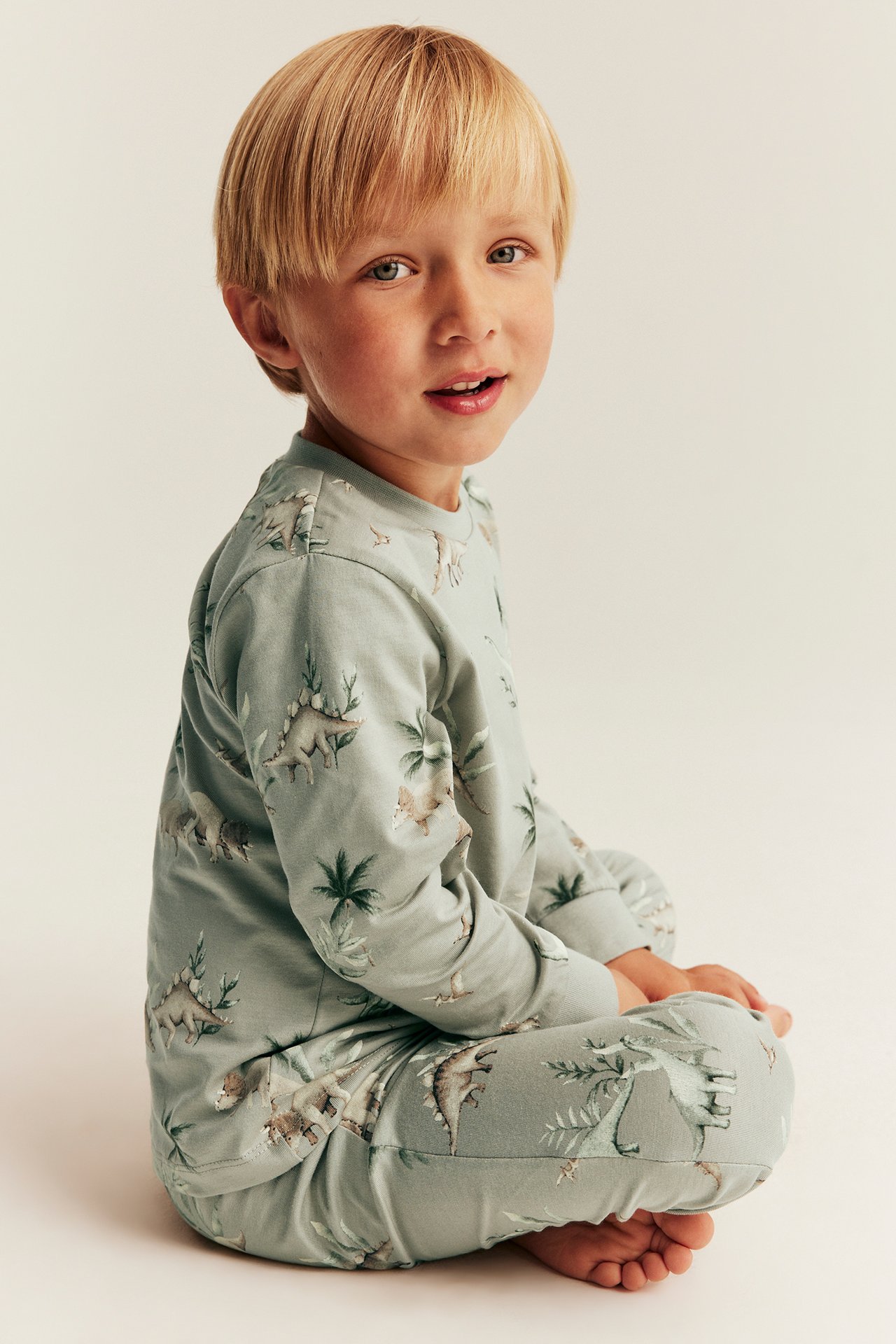 Seitenansicht eines Kindes in hellgrünem zweiteiligem Baumwollpyjama mit Dinosaurier-Muster.