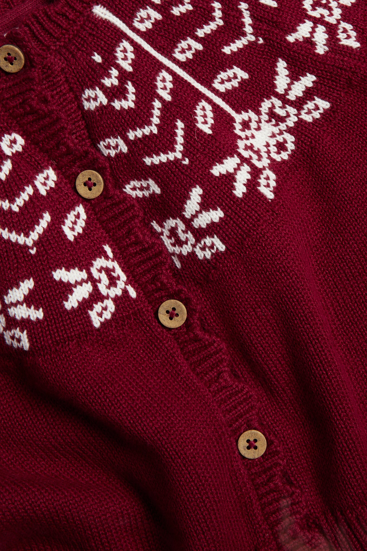 Nahaufnahme einer bordeauxroten Strickjacke mit weißem Fair-Isle-Muster und Holzknöpfen.