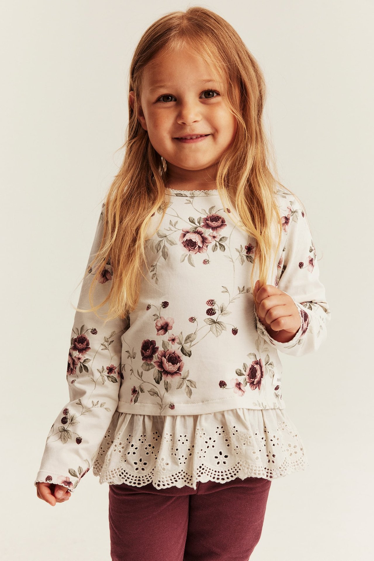 Vorderansicht eines Kindes in floralem Peplum-Langarmtop mit Spitzenbesatz und dunkelroten Leggings.
