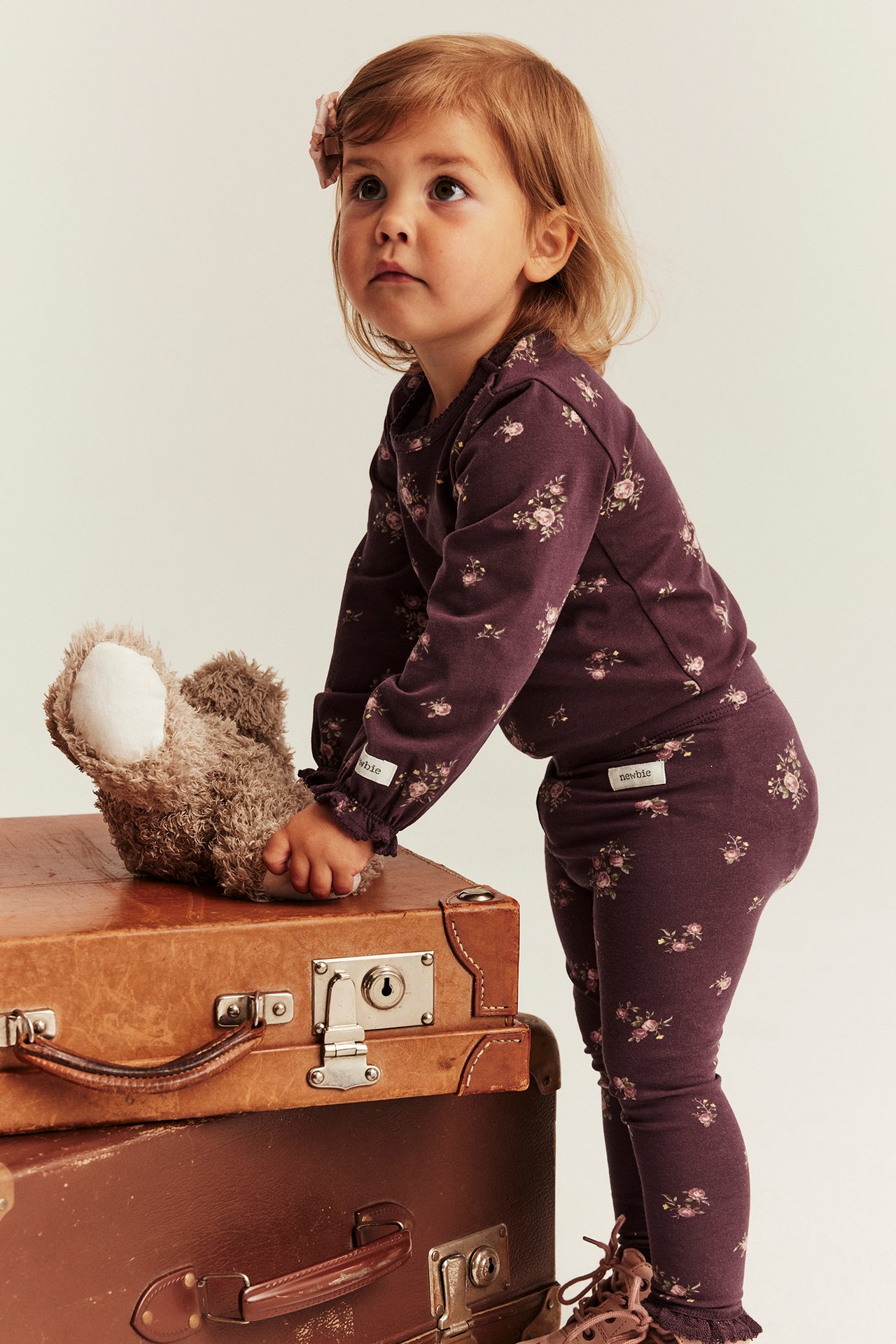 Kid in a dark purple floral long-sleeved top and matching leggings set, touching a teddy bear.