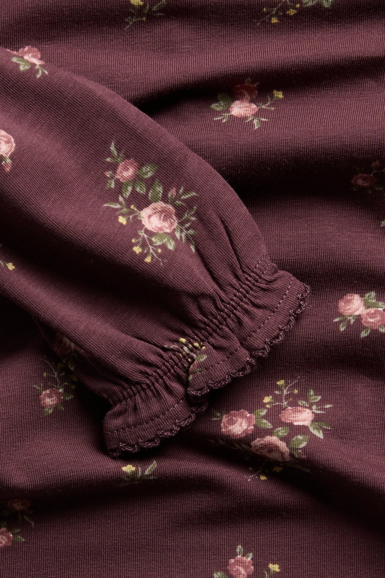 Close-up of a dark plum floral print garment sleeve with a ruffled cuff.