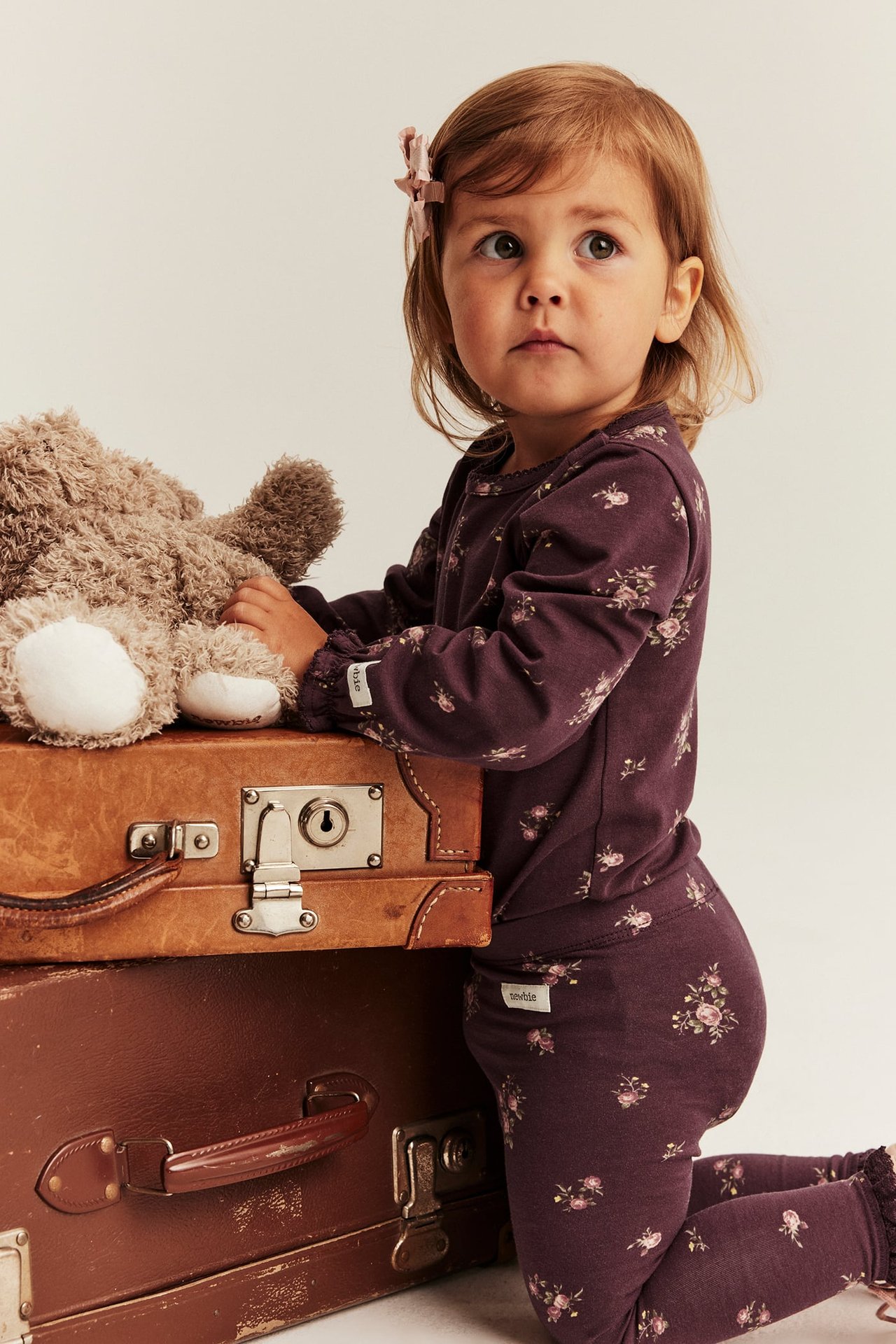 Seitenansicht eines Kindes in lila Blumenmuster-Langarmtop und Leggings-Set, mit Teddybär.
