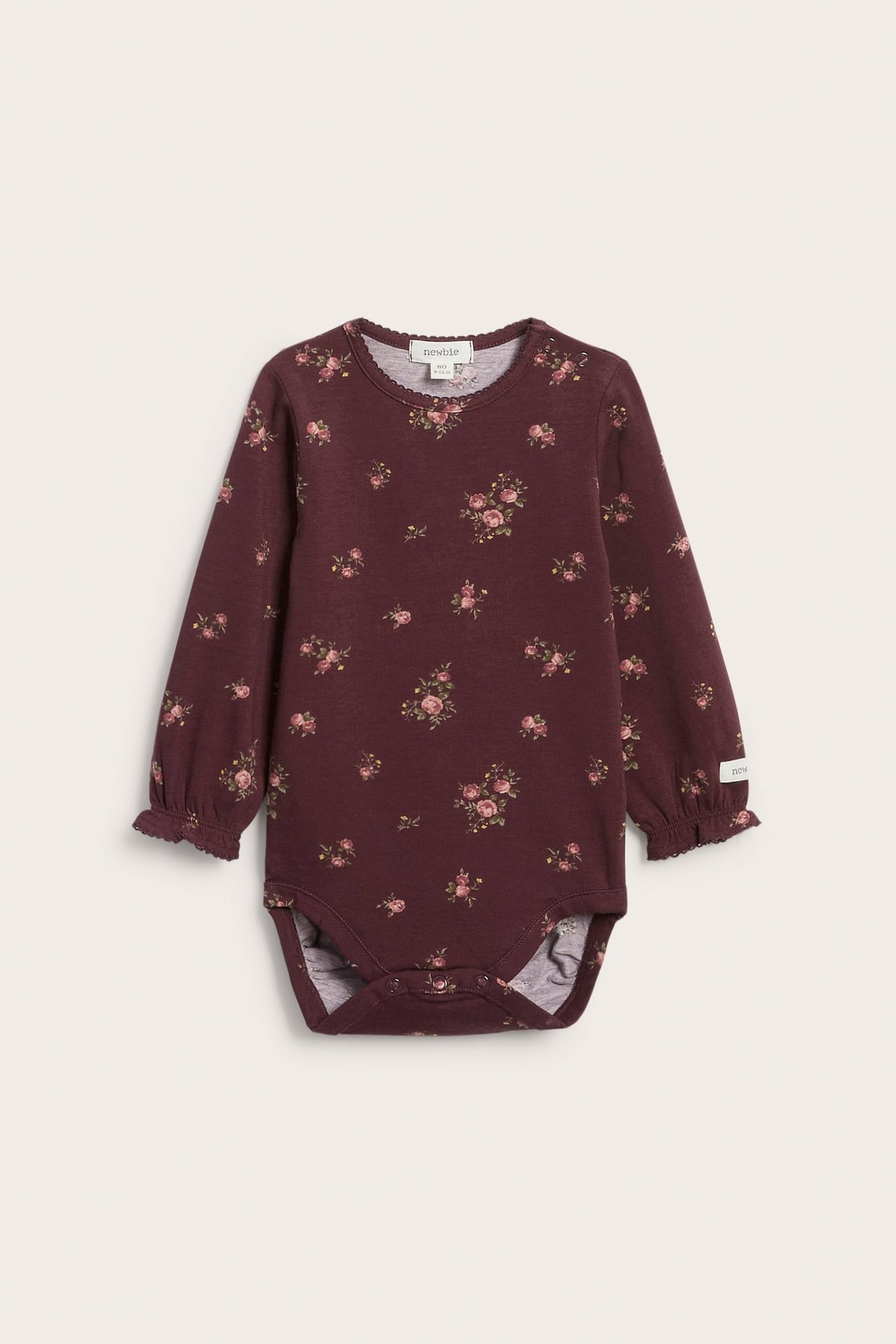 Vorderansicht eines baby bordeauxfarbenen Langarm-Bodysuits mit Blumenmuster und Rüschenbündchen.