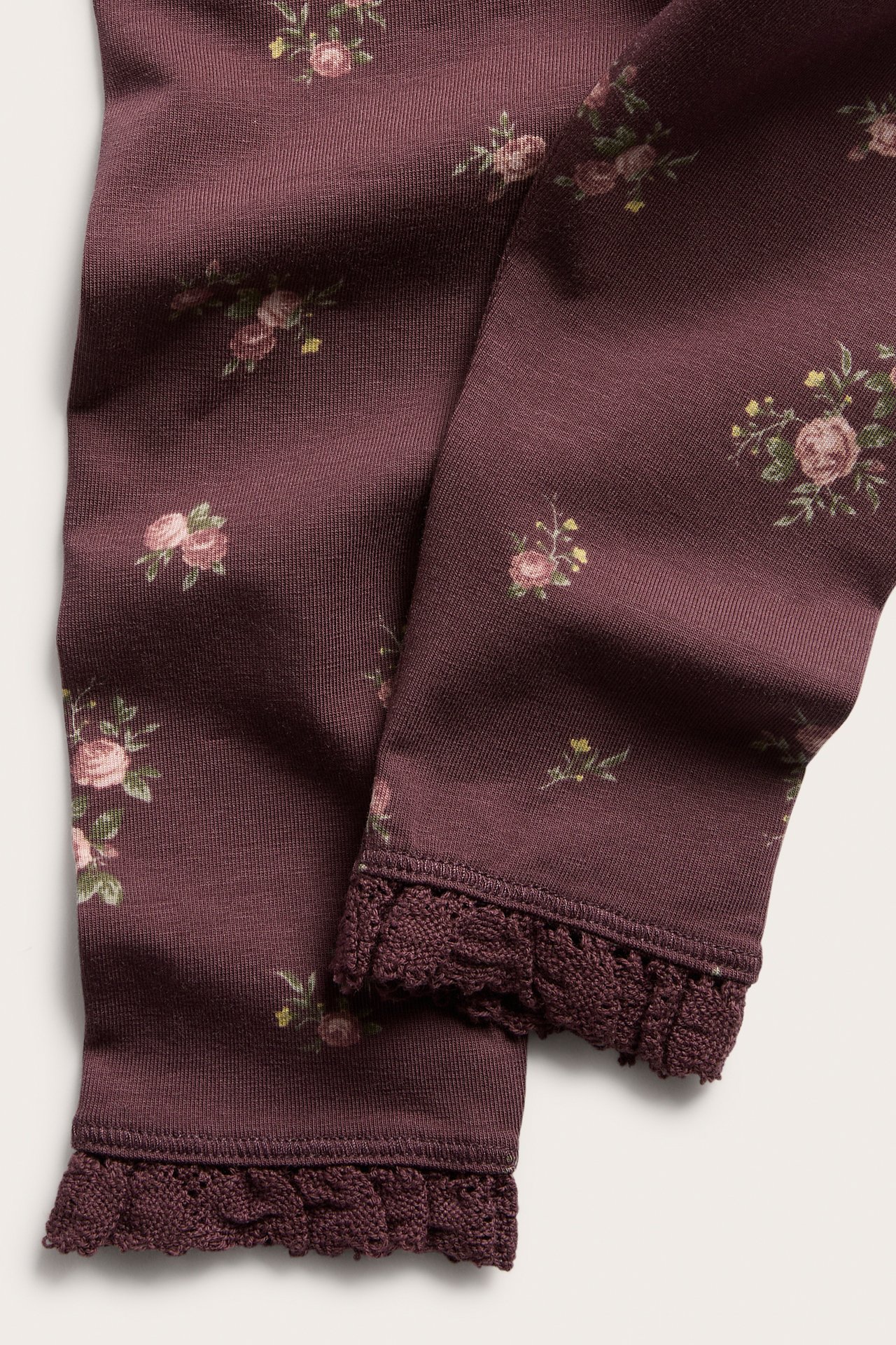 Close-up of plum floral print ribbed leggings with lace trim at the cuffs.