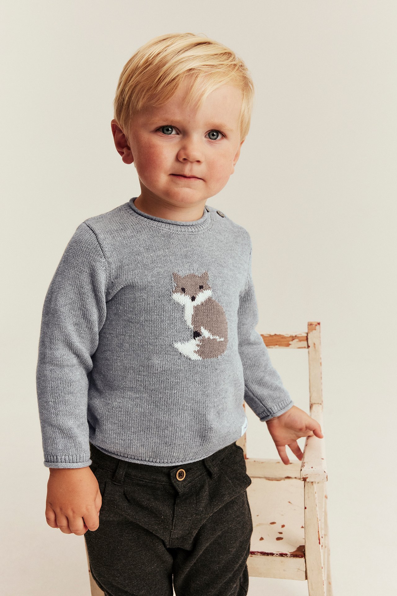 Vorderansicht eines Kindes in einem grauen Strickpullover mit Fuchsmotiv und dunkelgrauer Hose.