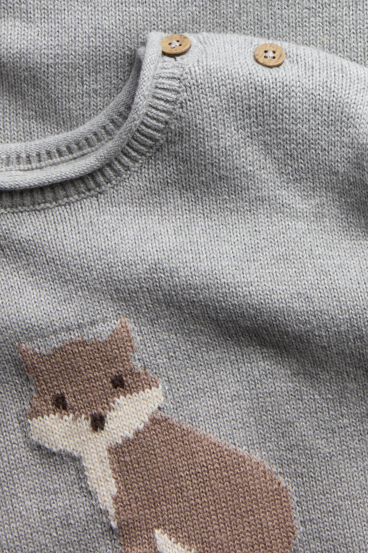 Close-up of a gray knitted baby sweater with a brown fox and wooden buttons.