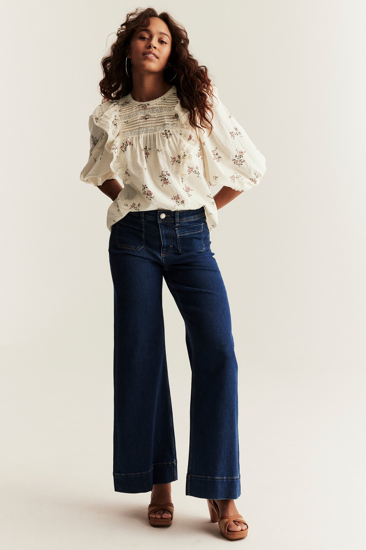 Off-white floral cotton blouse with ruffles and puff sleeves, dark blue wide-leg jeans, and brown sandals.