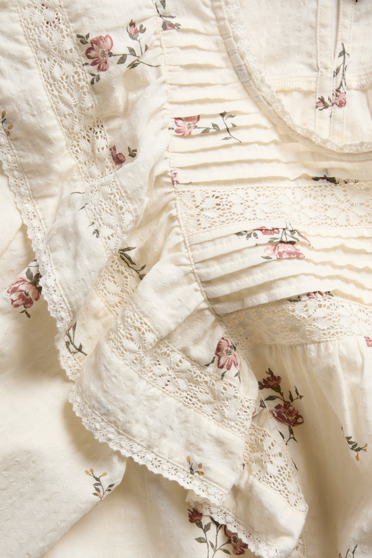 Close-up of an off-white cotton blouse with a floral pattern, lace trim, pintucks, and ruffles.