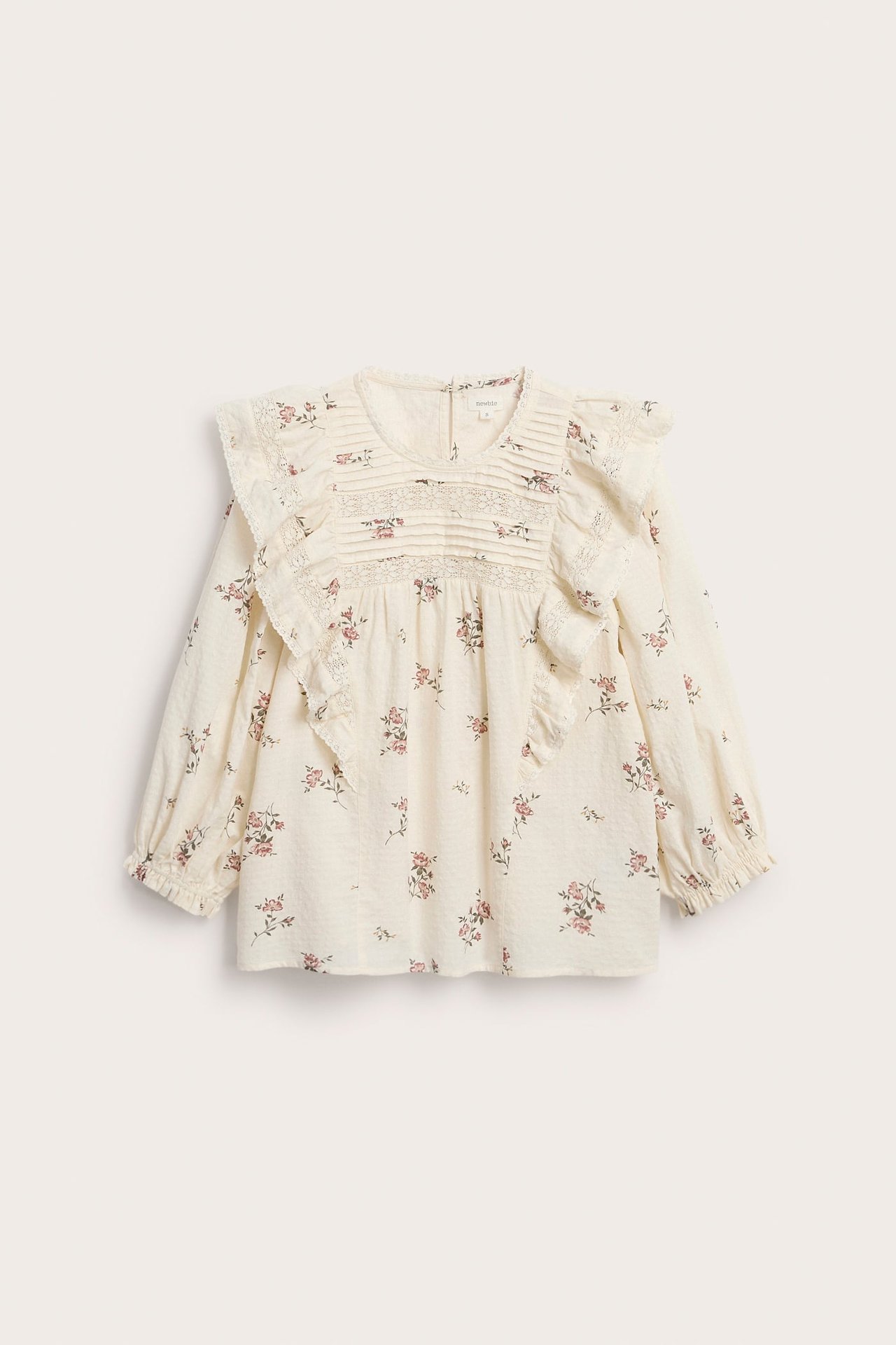 Front view of an offwhite floral cotton blouse with lace-trimmed ruffles, smocking, and 3/4 puff sleeves.