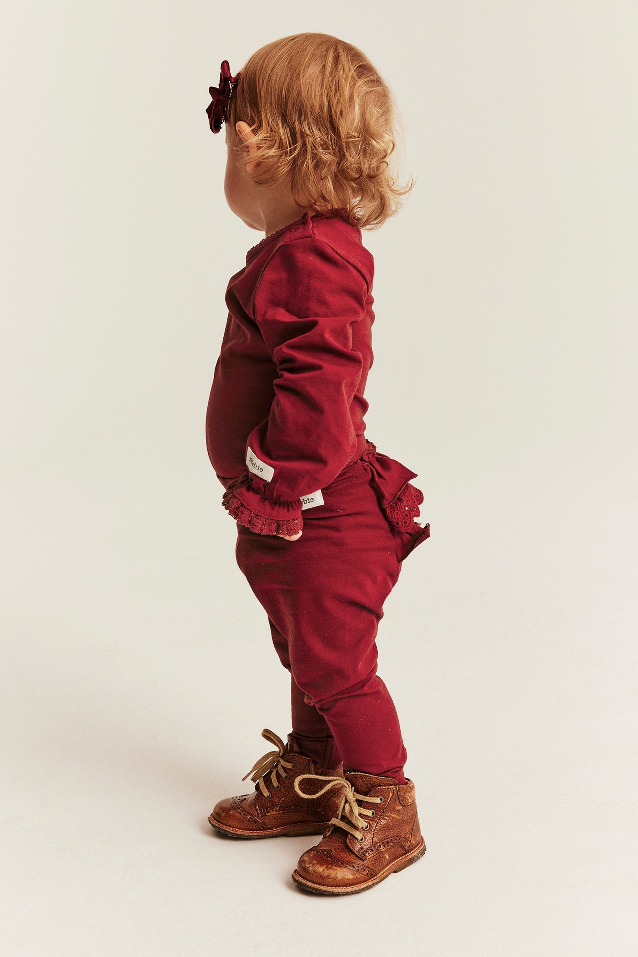 Baby in a red long-sleeved top with ruffled cuffs and matching ruffled pants, brown lace-up boots.