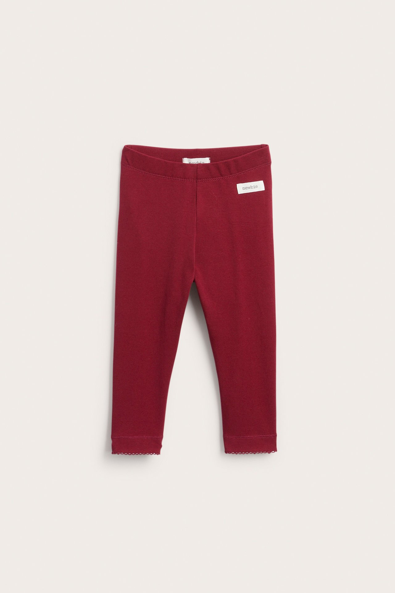 Front view of dark red baby leggings with scalloped cuffs and a small white tag.