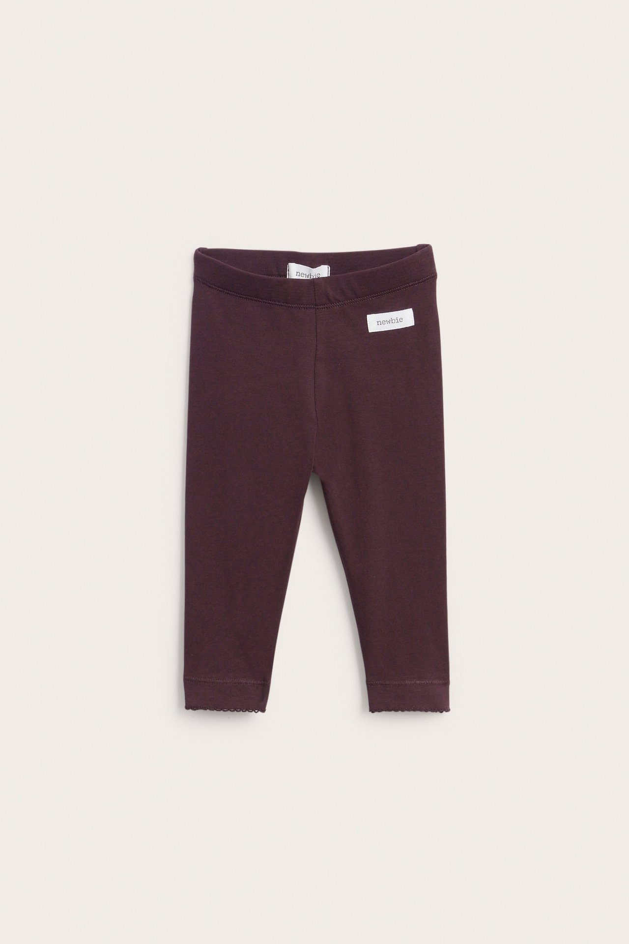Front view of dark plum baby leggings with a "newbie" label and scalloped ankles.