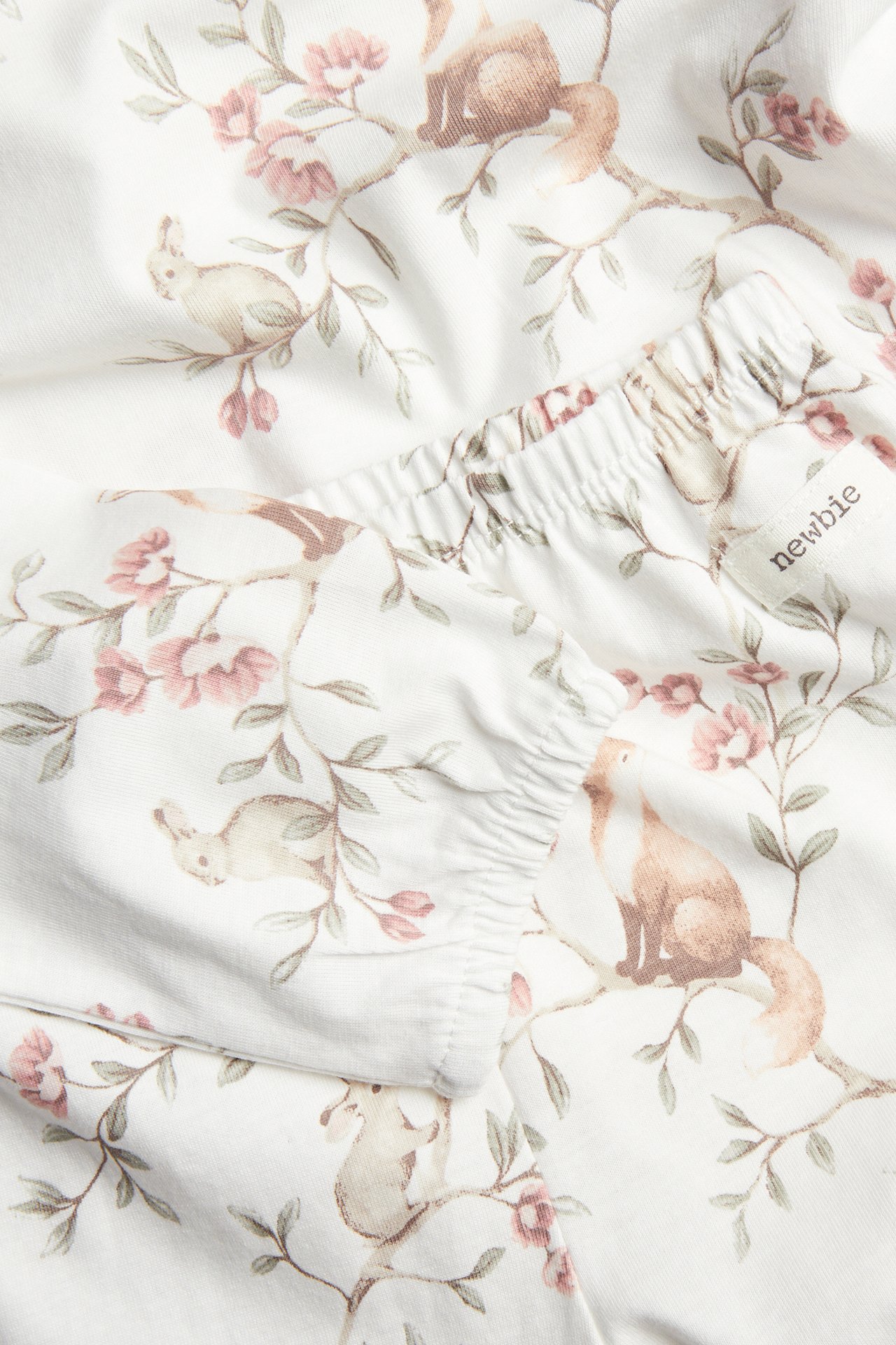 Nahaufnahme eines cremeweißen Baumwollpyjama-Sets mit Waldtier- und Blumenmuster, zeigt elastisches Saumdetail.