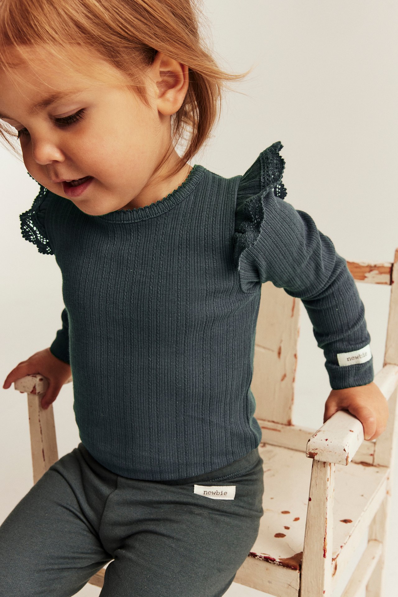 Baby in dunkelpetrolfarbenem geripptem Langarmshirt mit Rüschen und passenden Leggings.