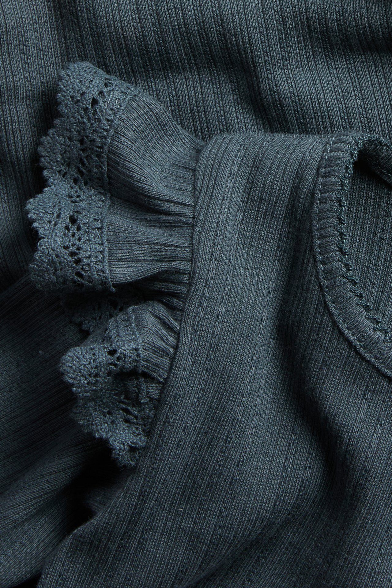Close-up of a dark teal ribbed top with lace-trimmed ruffled sleeves and a scalloped neckline.